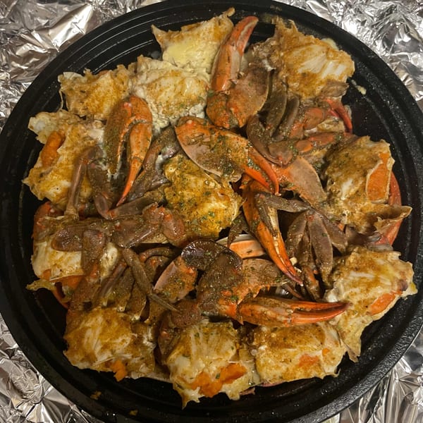 A black bowl filled with seasoned, cooked crab pieces and claws, ready to eat.