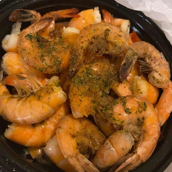 A close-up of Moruss Seafood's seasoned shrimp in a black bowl, garnished with herbs.