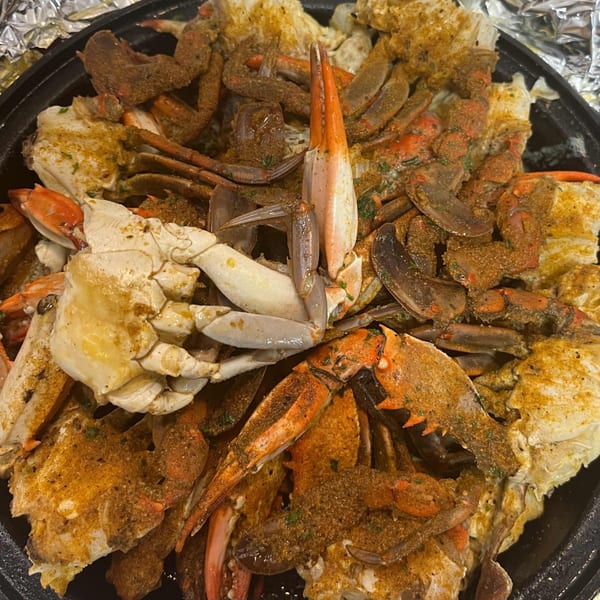 A close-up of a large platter filled with seasoned, cooked crabs, some with bright orange claws.