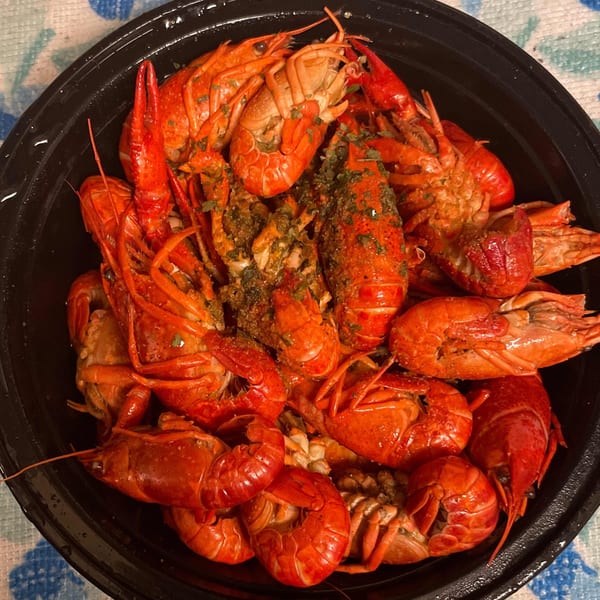 A black bowl filled with bright red, seasoned Moruss Seafood crawfish, ready to eat.